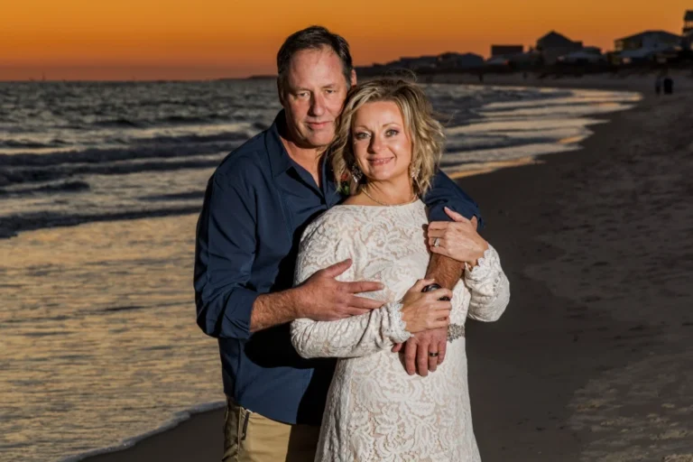 Bride and groom standing on the beach in front of a beautiful sunset in Gulf Shores, Alabama.