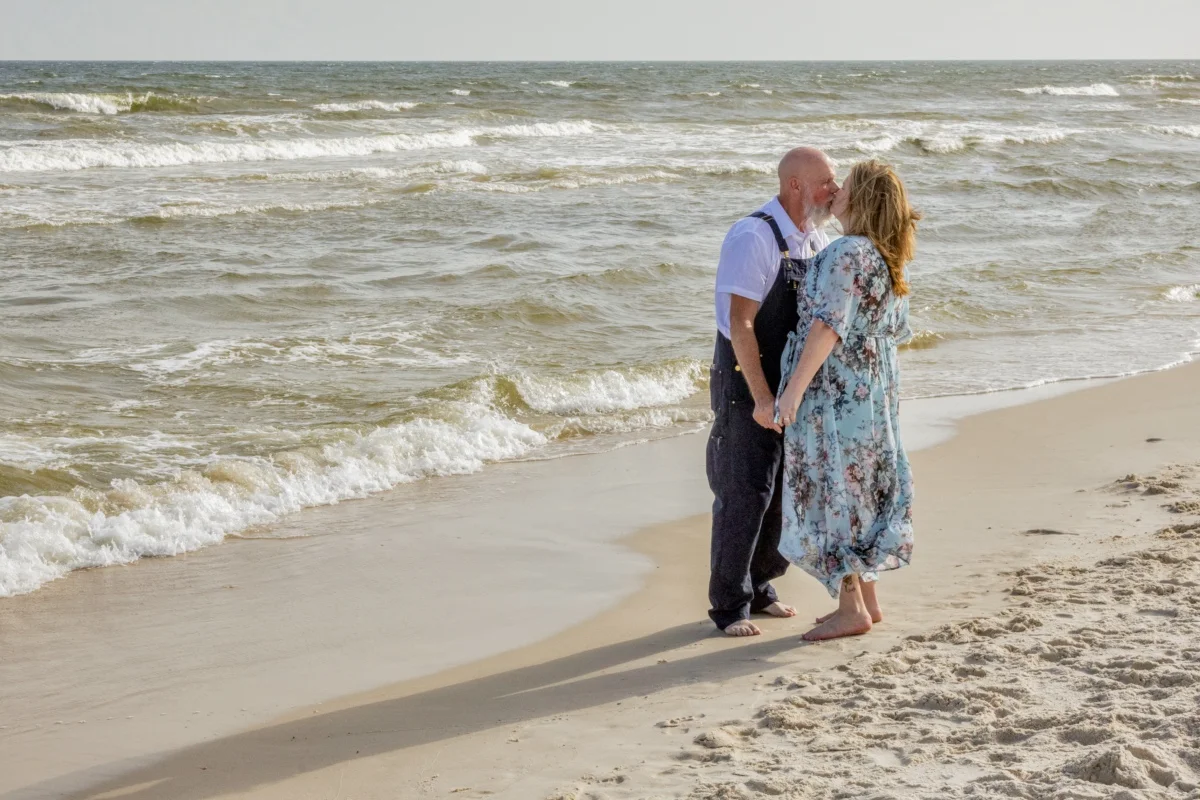Beach wedding couple kissing on the beach during a bright day wedding. 