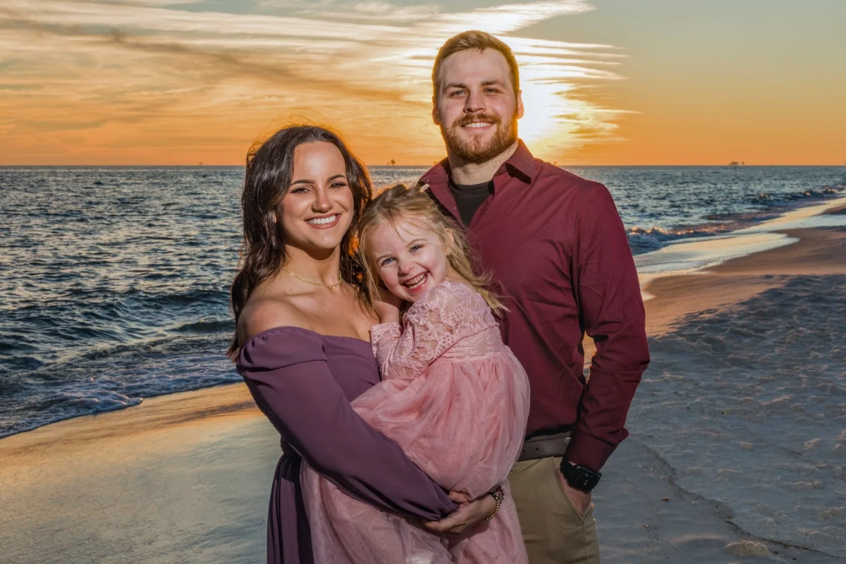Bride and groom with child standing in a beautiful sunset for a gulf shores beach wedding. Professional Photography 